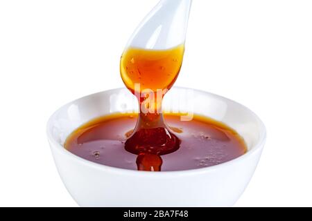 le miel s'écoule de la cuillère en céramique à la cuvette en céramique Banque D'Images