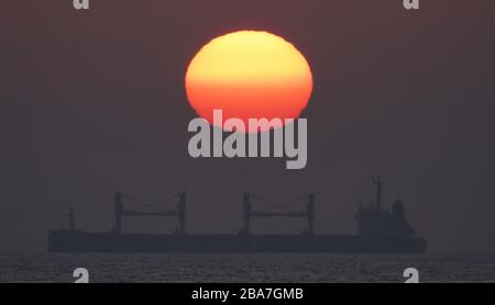 Le soleil se lève à travers la brume au-dessus du transporteur de vrac Legiony Polskie dans la mer du Nord au large de la côte de Whitley Bay sur la côte nord-est. Banque D'Images