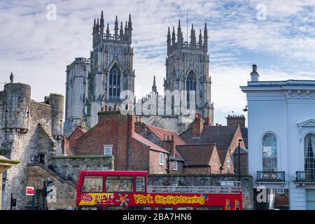 Un bus touristique rouge à impériale à toit ouvert stationné sur la place St Leonards, avec le bar Bootham et le distant York Minster, York, Royaume-Uni. Banque D'Images