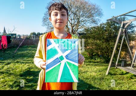 Un jeune garçon montre fièrement la peinture en acrylique sur toile qu'il a fait dans le jardin. Banque D'Images