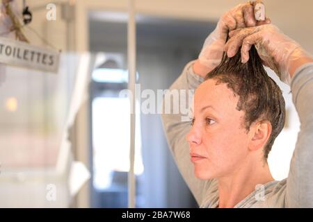 Une femme qui fait courir des teintures de cheveux aux bouts de ses cheveux bruns comme elle applique le colorant dans une vue rapprochée à la maison Banque D'Images