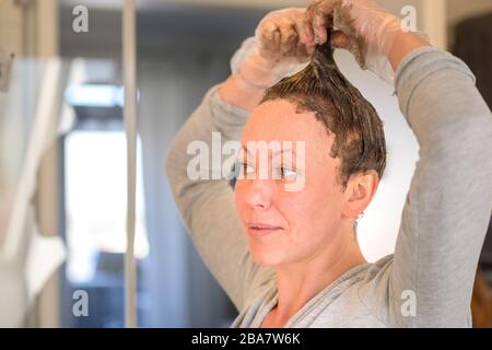 Une femme qui fait courir des teintures de cheveux aux bouts de ses cheveux bruns comme elle applique le colorant dans une vue rapprochée à la maison Banque D'Images