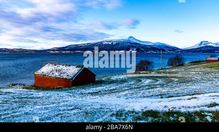 Haus am Meer, Tromsö, Bakkejord, Troms, Norwegen, bewölkter Himmel, montagnes enneigées, verschneite Berge, blauer Fjord, mer bleue, maison rouge, champ enneigé Banque D'Images