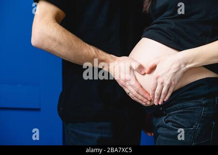 Gros plan de l'homme toucher le ventre de la femme enceinte. Pregeant femme et son mari qui font un coeur avec leurs mains sur son ventre. Banque D'Images
