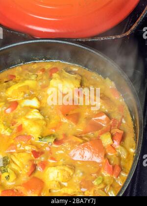 Curry composé de poivrons rouges de poisson blanc et de tomates qui se simmeraient dans une poêle sur une table de cuisson Banque D'Images