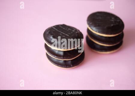 Une pile de gâteaux de Jaffa. Biscuits recouverts de chocolat noir et remplis de confiture de fraise rose ou de cerise. Délicieux biscuits isolés sur fond rose avec copyspace Banque D'Images