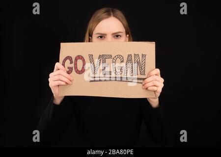 femme avec visage obscur tenant carton avec inscription go vegan isolée sur noir Banque D'Images