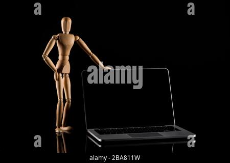 Poupée en bois en position debout avec la main sur la hanche près de l'ordinateur portable en noir Banque D'Images