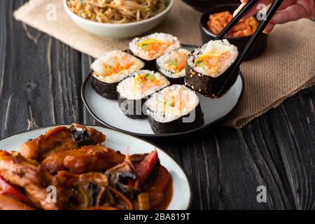 vue réduite d'une femme tenant des baguettes avec un rouleau de riz près des plats coréens Banque D'Images
