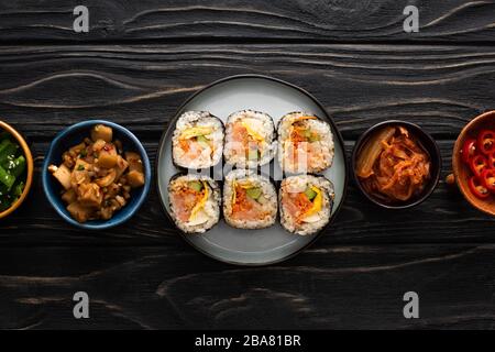 vue de dessus de la plaque avec gimbap près des plats latéraux dans des bols sur la surface en bois Banque D'Images