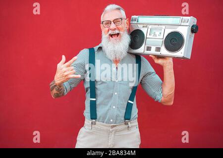 Un homme fou de haut niveau avec une chaîne stéréo boombox des années 80 jouant de la musique rock avec un fond rouge - un gars à la mode ayant une danse amusante avec une radio vintage - joyeux el Banque D'Images