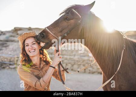 Jeune femme payeuse jouant avec son cheval dans une journée ensoleillée à l'intérieur du ranch corral - concept sur l'amour entre les gens et les animaux - se concentrer sur le visage de fille Banque D'Images