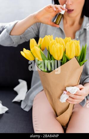 vue réduite d'une femme souffrant d'allergie au pollen, assise sur un canapé avec fleurs et contenant un spray nasal Banque D'Images