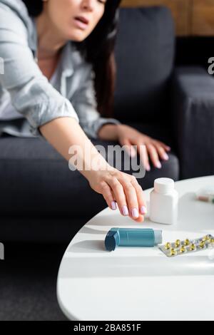 vue rognée de la femme atteignant l'inhalateur près de la plaquette thermoformée avec des pilules sur la table de café Banque D'Images