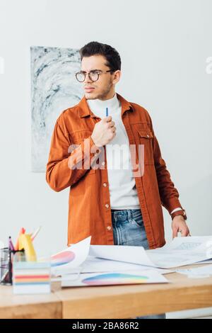 Point de mire sélectif du concepteur réfléchi tenant le marqueur près des cercles de couleur et des esquisses de conception de site Web sur la table Banque D'Images