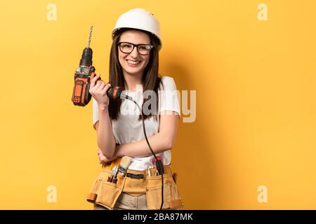 femme souriante dans un casque tenant la perceuse sur fond jaune Banque D'Images