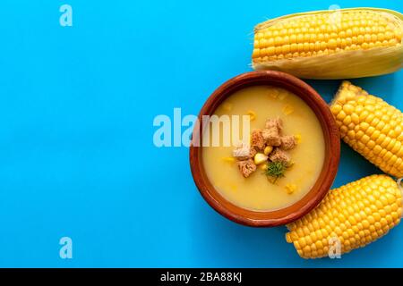 Soupe à la crème de maïs dans un bol marron avec du maïs doux frais sur fond bleu avec espace de copie. Vue de dessus. Banque D'Images