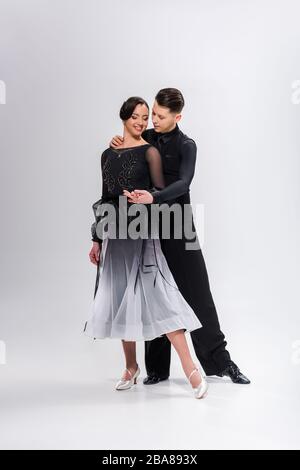 élégant couple jeune de danseurs de salle de bal en costume noir dansant sur blanc Banque D'Images