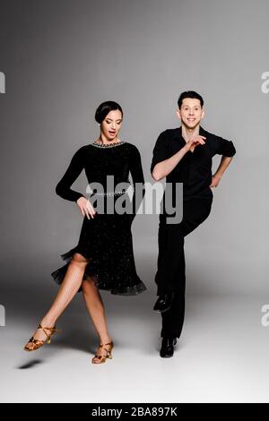 élégant couple jeune de danseurs de salle de bal en robe noire et danse de costume sur gris Banque D'Images