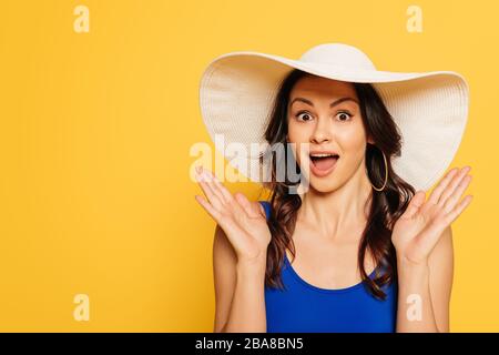 jolie, surprise femme dans un chapeau de soleil montrant un geste de wow isolé sur le jaune Banque D'Images
