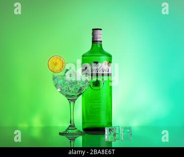 Cocktail tonique gin avec bouteille de gin, tranche de limon et de glace sur un miroir et fond vert avec espace de copie Banque D'Images