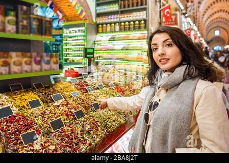 Belle femme montre des herbes séchées ou des fleurs en se tenant devant un stand d'épices vendu sur le stand en Egypte Bazar à Eminonu, Istanbul, Turquie Banque D'Images