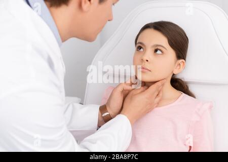 vue partielle de l'otolaryngologiste souriant touchant le cou de l'enfant mignon tout en examinant sa gorge Banque D'Images