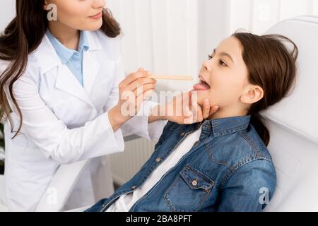 vue partielle de l'otolaryngologiste examinant la gorge de l'enfant avec le dépresseur de langue Banque D'Images