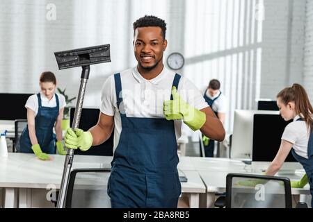 un aspirateur à brosse et un pouce près de l'équipe de collègues souriants d'afro-américains Banque D'Images