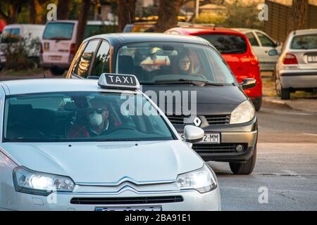 Chauffeur de taxi dans un citroën blanc portant un masque de protection lors de l'éclosion du virus corona. Femme inquiète dans la renault au loin Banque D'Images