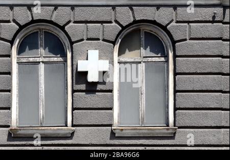 L'ancienne façade du XXIe siècle de l'hôpital de la ville. Deux fenêtres Art Nouveau et entre elles une croix blanche sur une cassette, vieux plâtre gris. Midi Banque D'Images