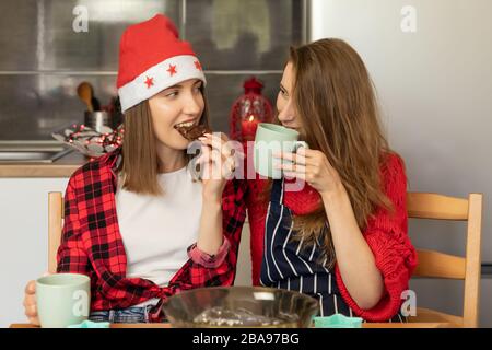 Deux jeunes filles préparent des biscuits de Noël à la maison dans la cuisine. Ils plaisantent et s'amusent, apprécient les corvées de vacances. Banque D'Images