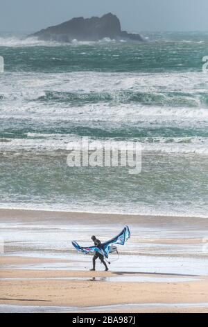 Un surfeur de kite solitaire a du mal à transporter son équipement de kite surf dans des vents forts sur la plage de Fistral à Newquay, dans les Cornouailles. Banque D'Images