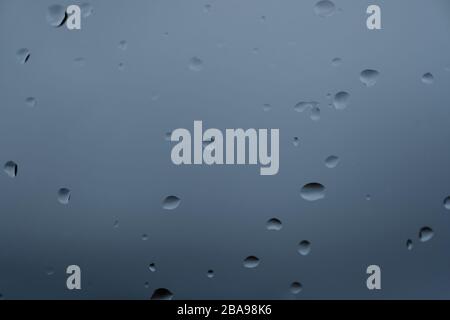 L'eau de pluie tombe sur le verre sur fond bleu flou, texture abstraite Banque D'Images