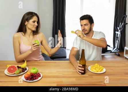 Un homme mène un mauvais style de vie, il mange des chips et de la bière. Le gars offre à la fille d'essayer des chips, mais elle refuse parce qu'elle mange bien et inquiète un Banque D'Images