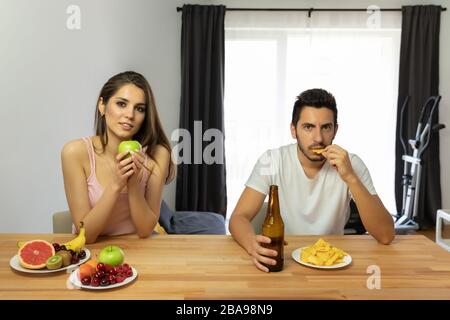 Un homme mène un mauvais style de vie, il mange des chips et de la bière. Le gars offre à la fille d'essayer des chips, mais elle refuse parce qu'elle mange bien et inquiète un Banque D'Images