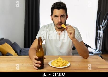 Un homme mène un mauvais style de vie, il mange des chips et boit de la bière. Dépendance à l'alcool, utilisation excessive de la restauration rapide. Banque D'Images