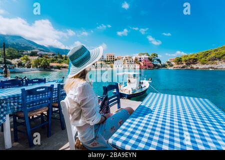 Vacances. Femme dans un café profitant du temps dans le village d'Assos en face de la baie émeraude du bateau blanc de mer méditerranéen et belle maison traditionnelle Banque D'Images