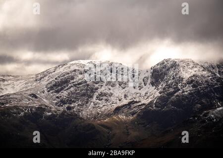 Gros plan du soleil se brisant à travers les nuages sur la neige couvert face orientale de NetherMost Pike, Lake District, Royaume-Uni Banque D'Images