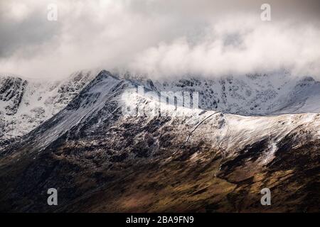 Gros plan du soleil qui traverse des nuages sur une arête enneigée qui mène au sommet couvert de nuages de Helvellyn, Lake District, Royaume-Uni Banque D'Images