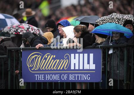 Les amateurs de course attendent que l'action commence devant la signalisation William Hill à l'hippodrome de Kempton Park Banque D'Images