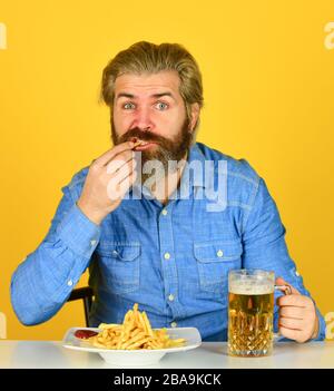 un homme paresseux qui aime la bière fraîche et la nourriture à l'eau. un homme qui mange vite. de la bière et des frites au restaurant. manger et boire au bar. hipster se détendre dans une taverne. un gars barbu qui sert des en-cas. Banque D'Images