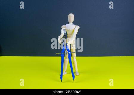 Figurine homme en bois avec compas sur la table jaune Banque D'Images