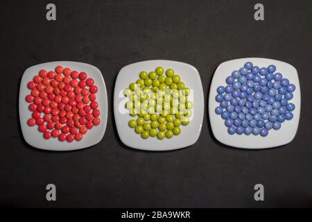 Avec trois plaques de chocolats bonbons colorés avec des couleurs RVB sur fond noir Banque D'Images