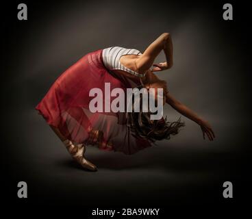 Ballerine. Jeune femme gracieuse danseuse de ballet, vêtue d'une tenue professionnelle, de chaussures et de jupe rouge haltérophile, fait preuve d'habileté à danser. Beauté o Banque D'Images