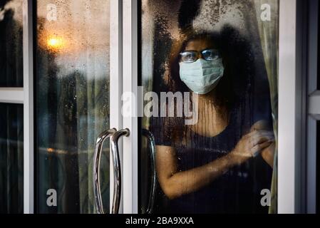 Femme regardant par la fenêtre humide pendant le séjour à la maison pendant que COVID-19 Banque D'Images