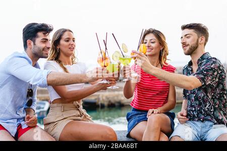 Des amis dégustant des cocktails de fruits tropicaux mélangés, disent des encouragements. Les jeunes qui se amusent à boire et à encourager ensemble le concept de style de vie. Banque D'Images