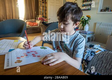 Un jeune garçon coloriant dans des formes impaires numérotées dans le cadre d'un exercice de scolarité à la maison. Il apprend de la maison en raison du coronavirus. Banque D'Images