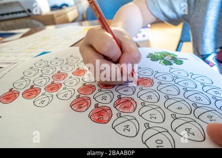 Vue rapprochée de la main d'un jeune enfant utilisant un crayon de couleur pour colorer en nombres impairs dans le cadre d'une éducation à la maison en raison de la pandémie de coronavirus. Banque D'Images