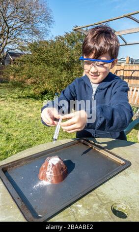 Un jeune garçon fait une expérience scientifique dans le jardin mélangeant le vinaigre et le bicarbonate de soude pour simuler une éruption volcanique. Banque D'Images